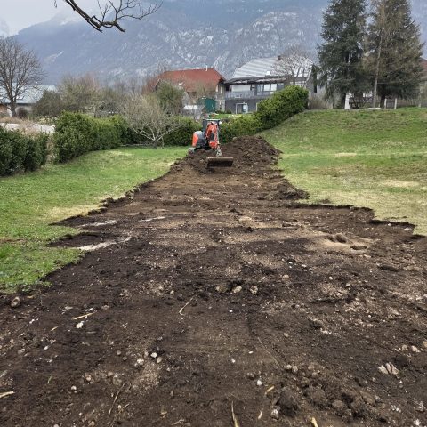 Workers digging a trench in a grassy area with mountains in the background.